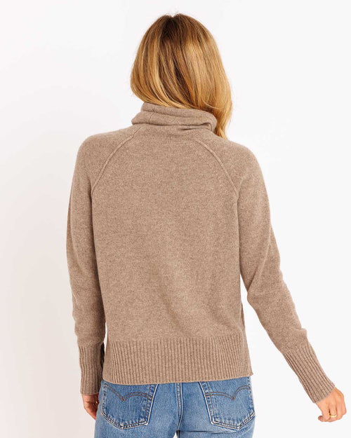 LIFESTYLE / EDITORIAL: Woman wearing a driftwood-colored cashmere funnel neck sweater, back view, paired with blue jeans