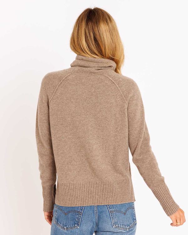 LIFESTYLE / EDITORIAL: Woman wearing a driftwood-colored cashmere funnel neck sweater, back view, paired with blue jeans