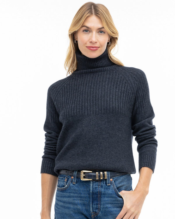 Woman wearing charcoal half-rib turtleneck cashmere sweater tucked into blue jeans with black belt