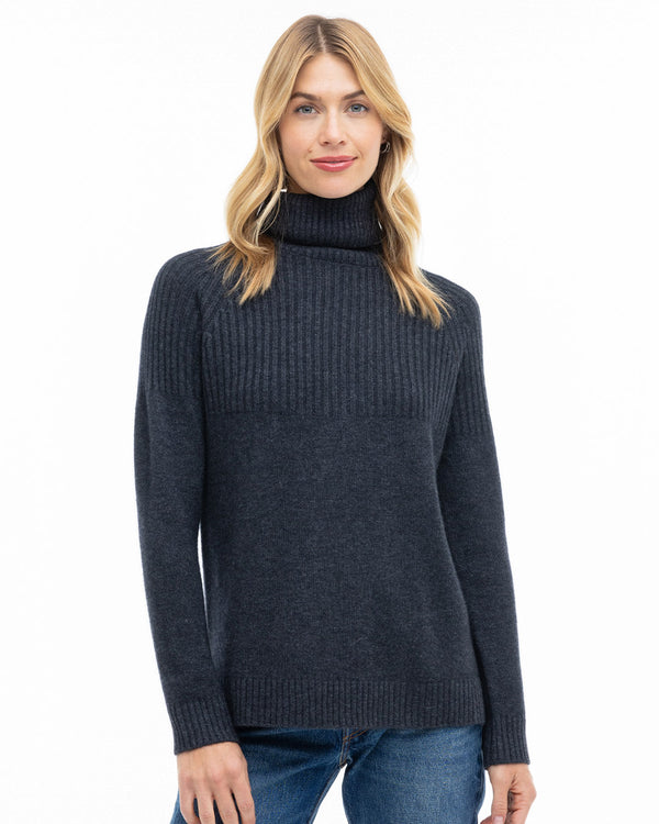 Front-facing image of a woman wearing a charcoal half-rib turtleneck cashmere sweater and blue jeans.