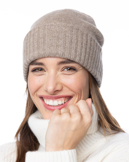 LIFESTYLE / EDITORIAL: Smiling woman wearing beige cashmere beanie and white turtleneck sweater against white background