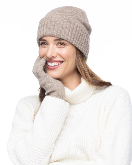 Woman wearing beige cashmere hat and gloves with white cashmere turtleneck sweater, smiling against white background