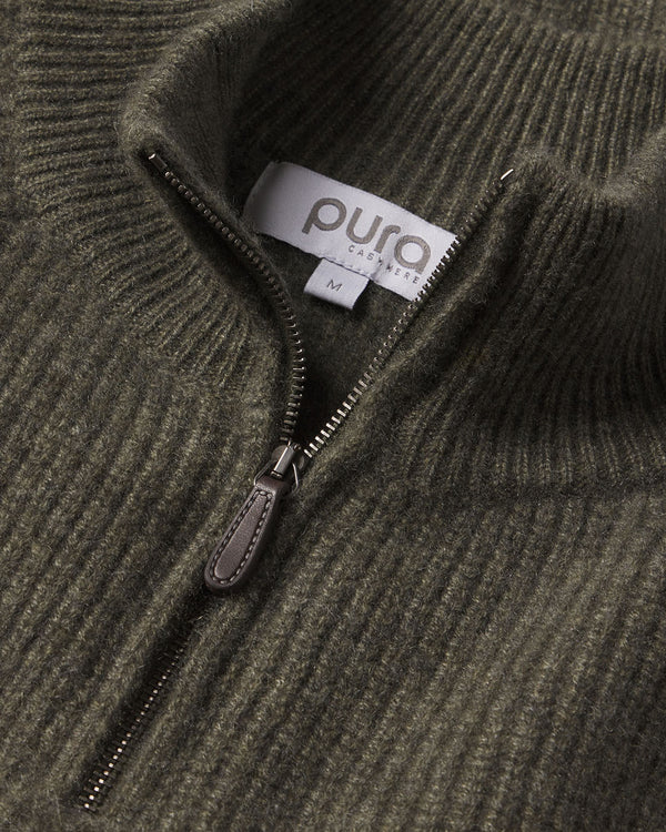 Close-up of dark olive ribbed cashmere fabric with a half-zip and "puro cashmere" label, size M visible