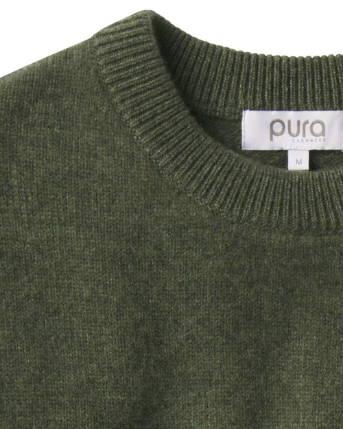 Close-up of dark olive green cashmere crew neck sweater with ribbed collar and visible brand label "pura essence
