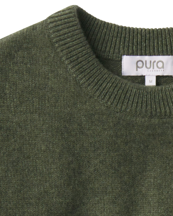 Close-up of dark olive green cashmere crew neck sweater with ribbed collar and visible brand label "pura essence
