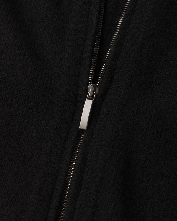 Close-up of black cashmere fabric with partially zipped silver zipper on a zip-up cardigan