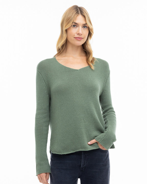 Woman wearing olive green V-neck cashmere sweater and dark pants against white background