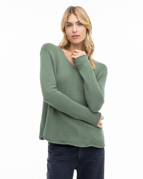 Woman wearing olive green round neck cashmere sweater with long sleeves and dark pants against white background