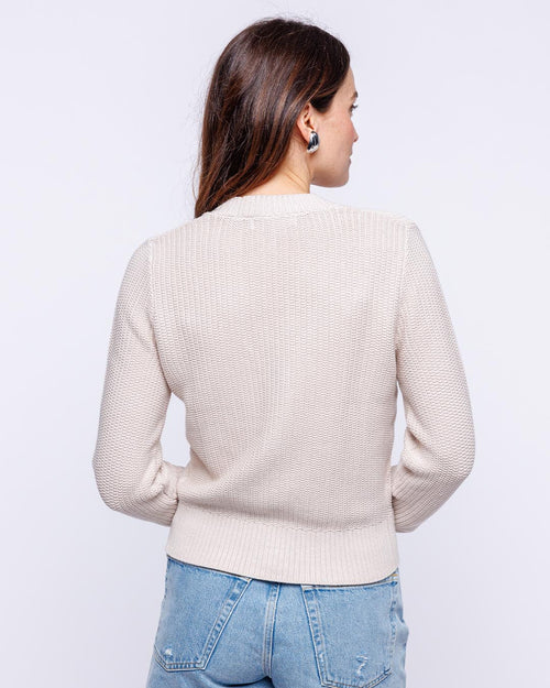 LIFESTYLE / EDITORIAL: Woman wearing oatmeal textured cardigan and light blue jeans, shown from back against white background