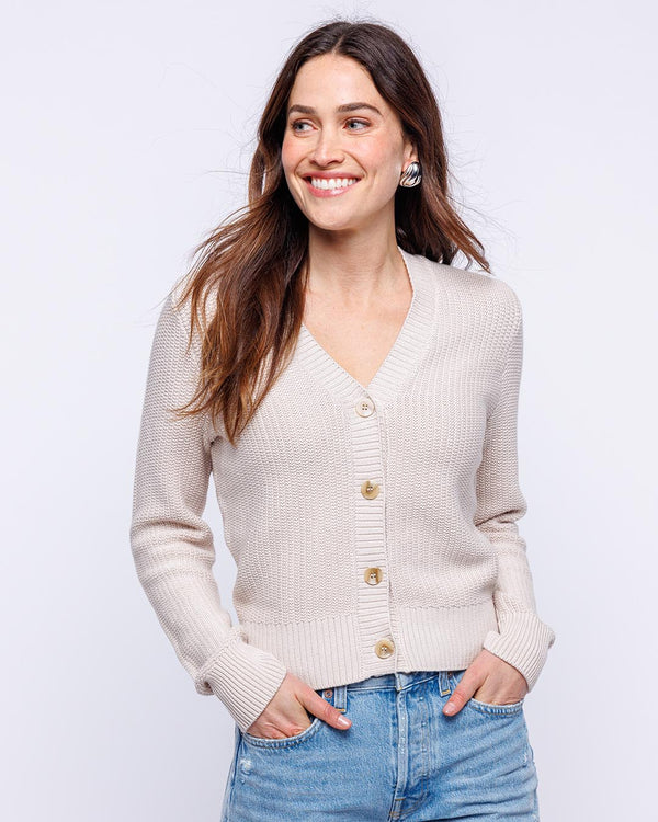 LIFESTYLE / EDITORIAL: Woman wearing oatmeal-colored textured cardigan and blue jeans, smiling against a white background