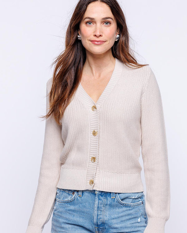 LIFESTYLE / EDITORIAL: Woman wearing oatmeal textured cardigan with buttons and blue jeans against white background