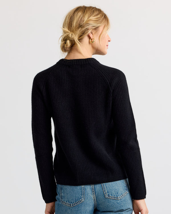 LIFESTYLE / EDITORIAL: Woman with blonde hair in low bun wearing black cashmere sweater and blue jeans, back view
