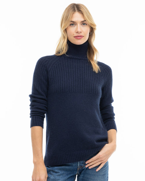 LIFESTYLE / EDITORIAL: Woman wearing navy blue turtleneck cashmere sweater and jeans, standing against white background