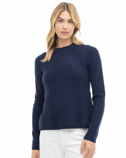 Front view image of a woman wearing a navy ribbed cashmere sweater with white pants against a white backdrop