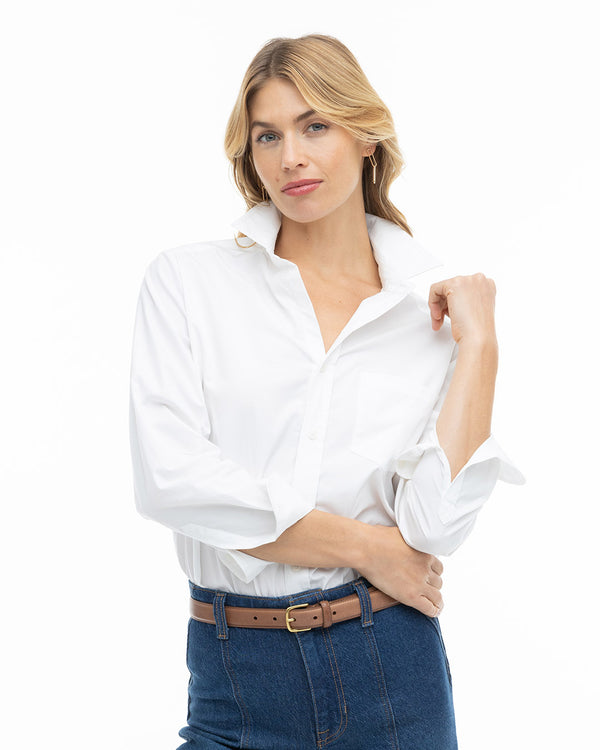 LIFESTYLE / EDITORIAL: Woman wearing white button-up shirt tucked into high-waisted blue jeans with a brown belt, posing
