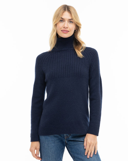 LIFESTYLE / EDITORIAL: Woman wearing navy ribbed turtleneck cashmere sweater and blue jeans against white background