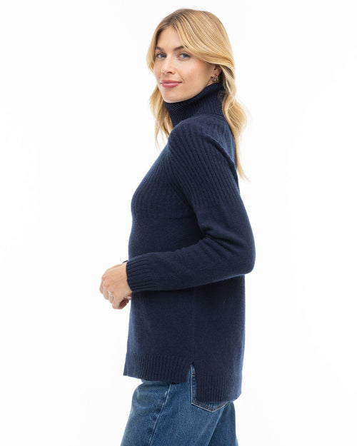 LIFESTYLE / EDITORIAL: Woman in navy turtleneck cashmere sweater and jeans, side view, white background