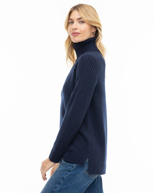 Side profile image of a woman wearing a navy blue turtleneck cashmere sweater and jeans against white background