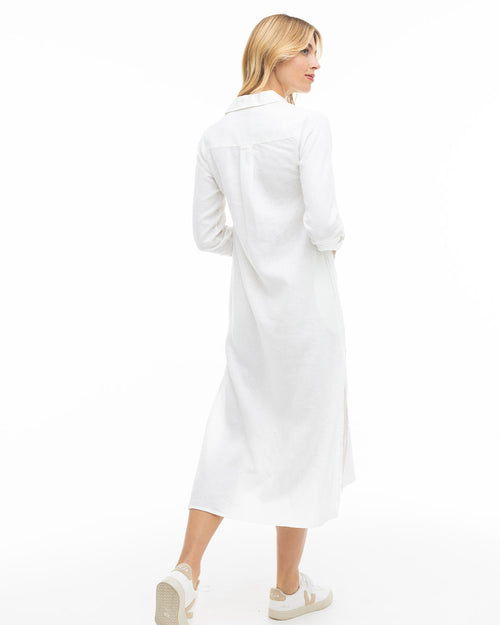 Woman in white long shirt dress and white sneakers, standing with back to camera on white background