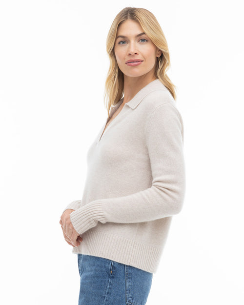 Woman wearing oatmeal-colored cashmere sweater with collar, paired with blue jeans, against white background