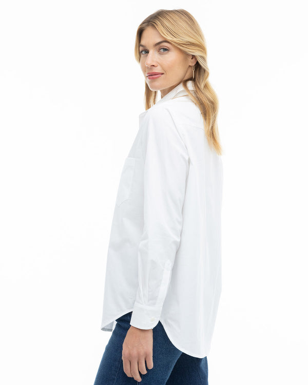 Woman in white classic button-up shirt and blue jeans, side view, against white background