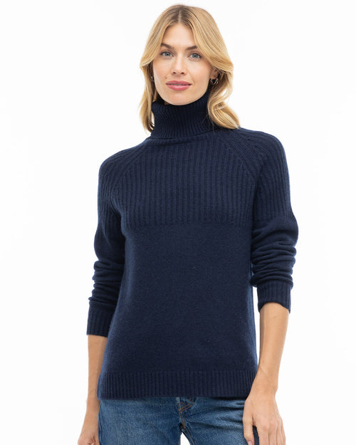 Front view image of a woman wearing a navy blue turtleneck cashmere sweater with jeans against white background