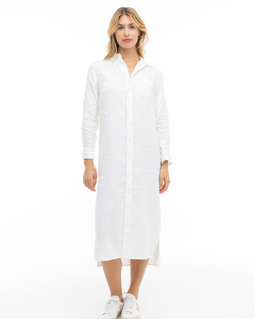 LIFESTYLE / EDITORIAL: Woman wearing a long white button-down dress and white sneakers, standing against a white background