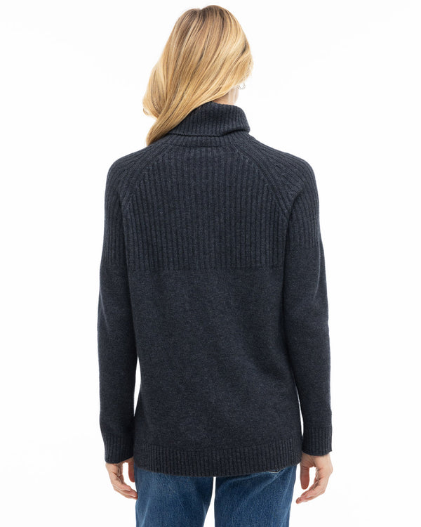 Rear view image of a woman wearing a charcoal ribbed turtleneck cashmere sweater with blue jeans on white background