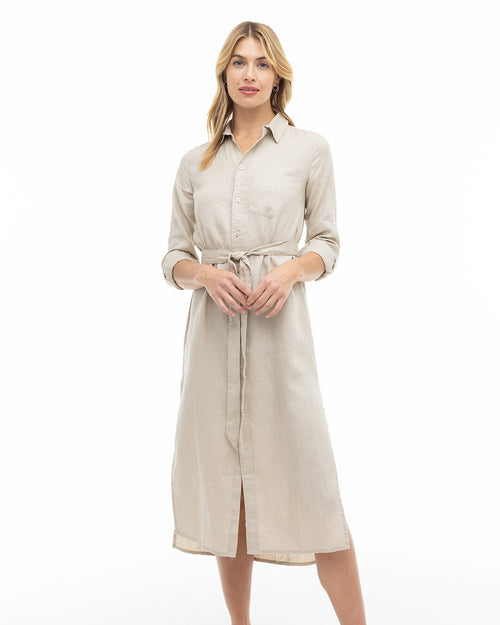 LIFESTYLE / EDITORIAL: Woman wearing a sandstone-colored long shirt dress with rolled sleeves and a waist tie, standing