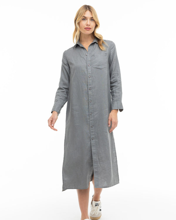 Woman wearing long graphite gray button-up dress with collar and sneakers, standing against white background