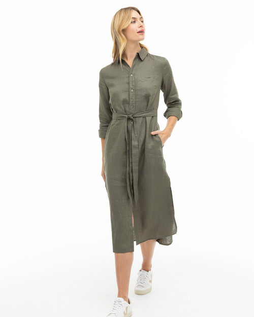 LIFESTYLE / EDITORIAL: Woman wearing dark olive shirt dress with belt and white sneakers walking against white background