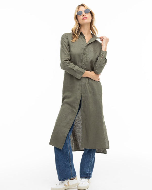 LIFESTYLE / EDITORIAL: Woman wearing dark olive long shirt dress over jeans and white sneakers with sunglasses on white