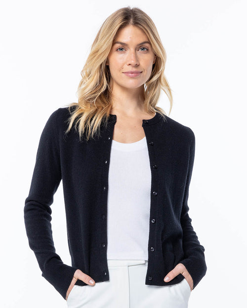 LIFESTYLE / EDITORIAL: Woman wearing black button-up cashmere cardigan over white top, hands in pockets, white background