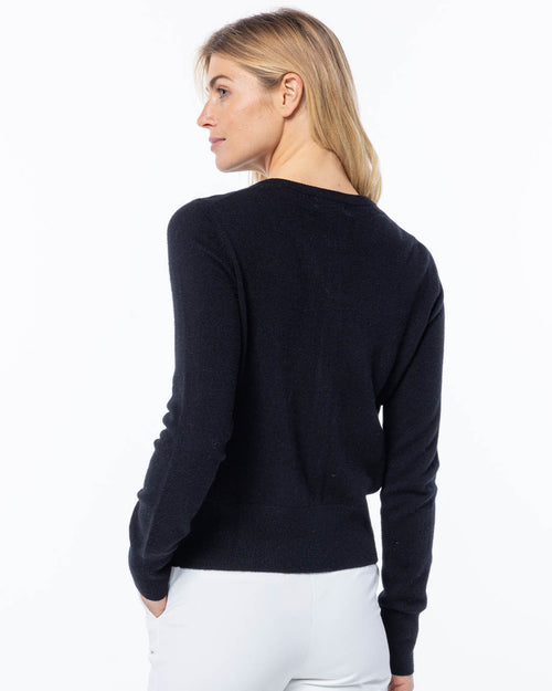 LIFESTYLE / EDITORIAL: Woman in black cashmere sweater, side profile, hands in pockets, white pants, plain background