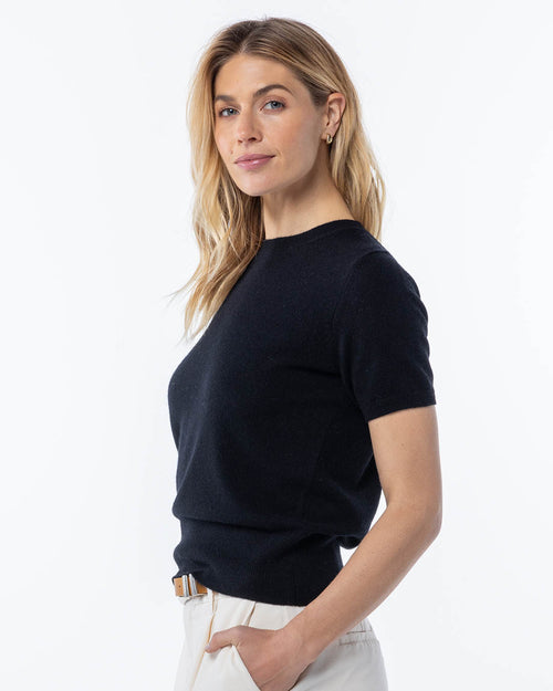 LIFESTYLE / EDITORIAL: Woman wearing black short-sleeve cashmere sweater, standing sideways with hand in pocket against
