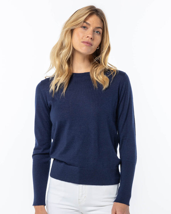 Front-facing image of a woman wearing a navy blue cashmere sweater paired with white pants against white background
