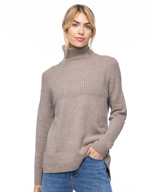 Woman wearing vintage khaki half-rib turtleneck cashmere sweater with blue jeans, standing against white background