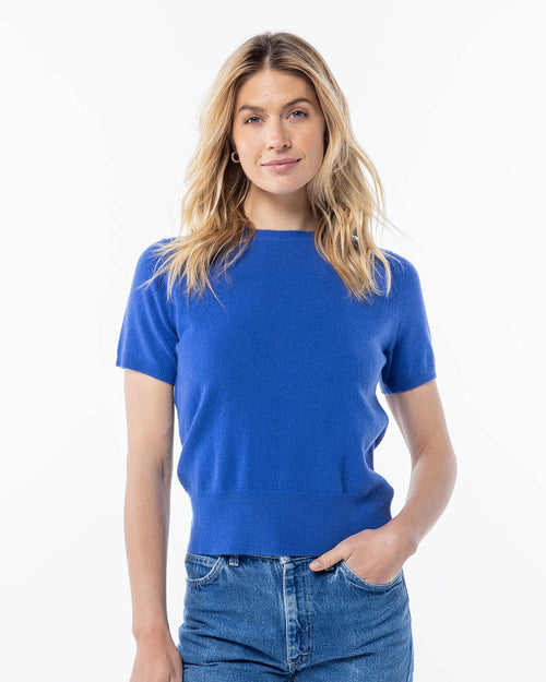 LIFESTYLE / EDITORIAL: Woman wearing a French blue short-sleeve cashmere sweater and jeans, standing against white background