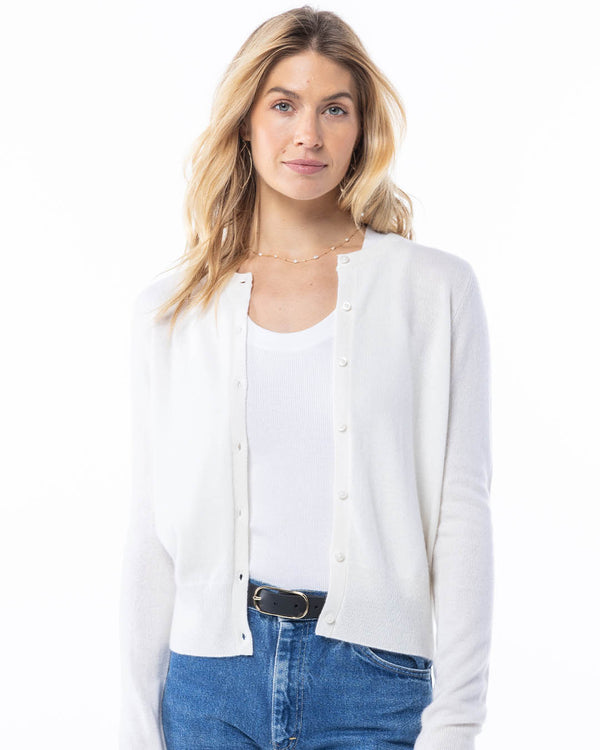 Front-facing image of a woman wearing a white cashmere cardigan paired with a white tank top and blue jeans