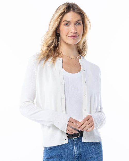 Front-facing image of a woman wearing a white cashmere cardigan over a white tank top and blue jeans
