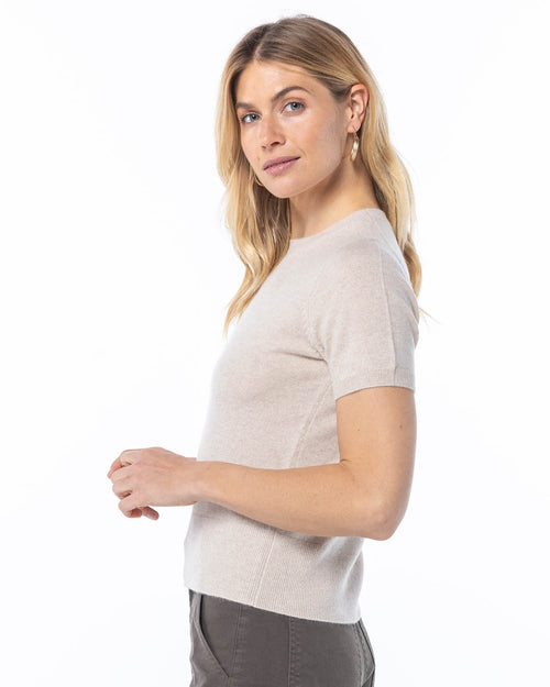 Woman wearing short-sleeve oatmeal cashmere sweater, side view, against white background