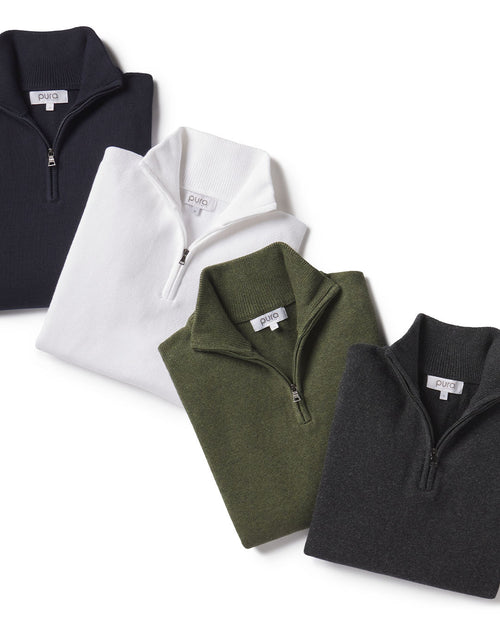 Four folded quarter-zip cashmere sweaters in black, white, olive green, and dark gray on white background
