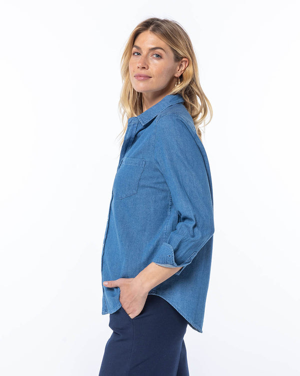 Woman in medium wash blue denim shirt and dark pants, side view, white background, casual pose