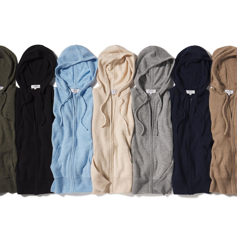 Seven folded cashmere zip-up hoodies in various colors laid flat, showcasing texture and hood details.