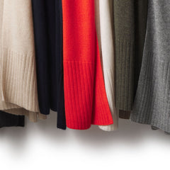 Close-up of hanging cashmere travel wraps in beige, navy, red, cream, olive, and gray colors