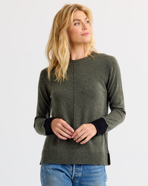 LIFESTYLE / EDITORIAL: Woman wearing dark olive cashmere sweater with black cuffs and blue jeans, looking to side