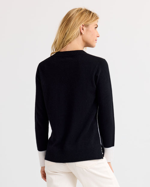 Woman wearing black cashmere sweater with white cuffs, viewed from the back against a plain white background