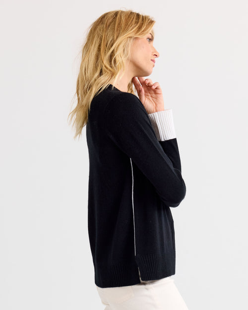 LIFESTYLE / EDITORIAL: Side view of woman wearing black and white cashmere sweater against plain background