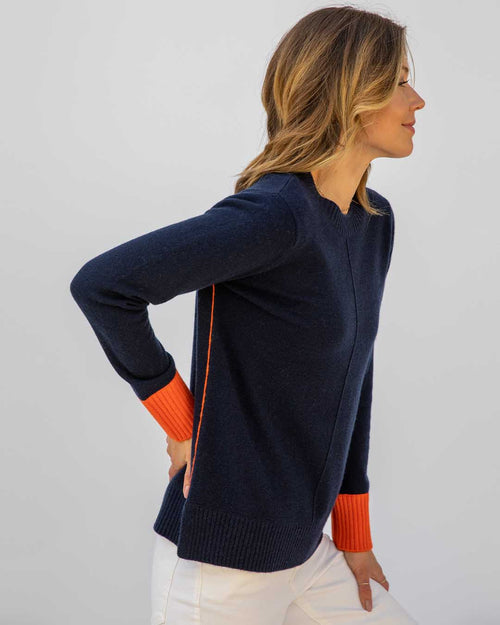 LIFESTYLE / EDITORIAL: Woman in navy cashmere sweater with orange cuffs and piping, wearing white pants, side profile view