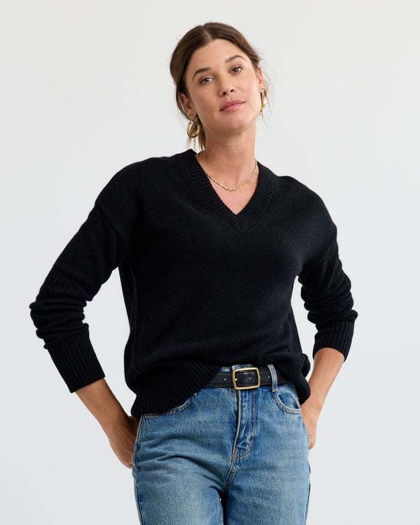 LIFESTYLE / EDITORIAL: Woman wearing black V-neck cashmere sweater and blue jeans with hands in pockets against white